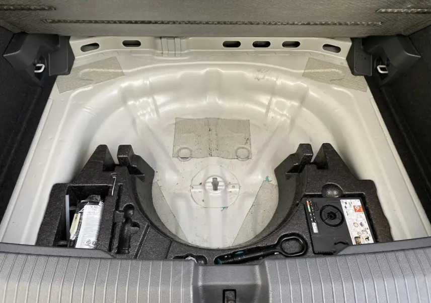 Vue du coffre ouvert d'un Volkswagen T-Roc 2024 gris, montrant le rangement sous plancher sans roue de secours.