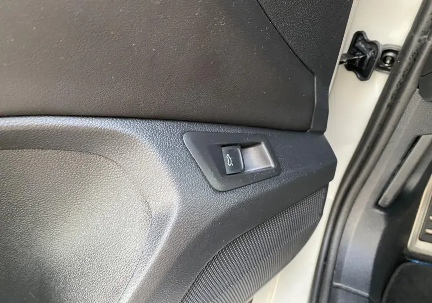 Détail du bouton d'ouverture du coffre sur la porte côté conducteur d'un Volkswagen T-Roc gris 2024.