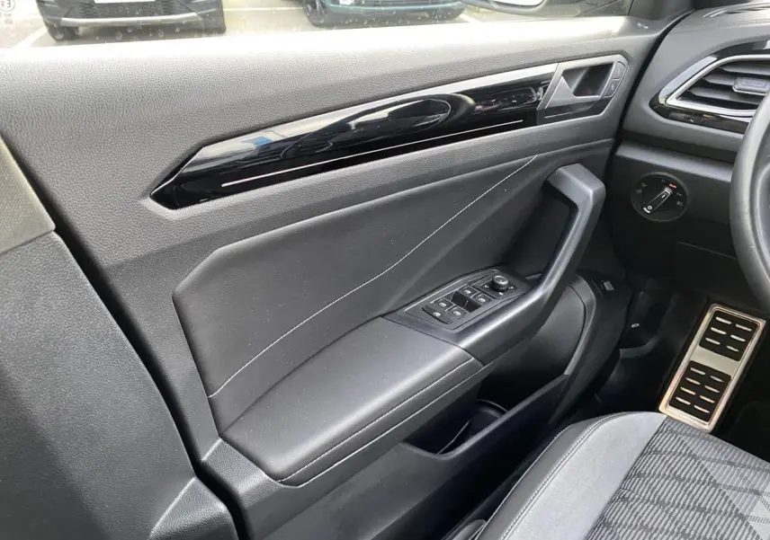 Intérieur côté conducteur du Volkswagen T-Roc 2024, porte noire avec commandes des vitres et pédalier en acier brossé.