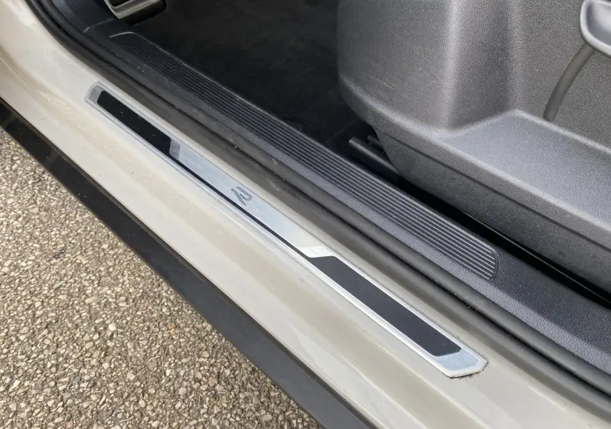 Gros plan sur la plaque de seuil de porte R-Line d'un Volkswagen T-Roc gris, côté conducteur, avec intérieur noir.