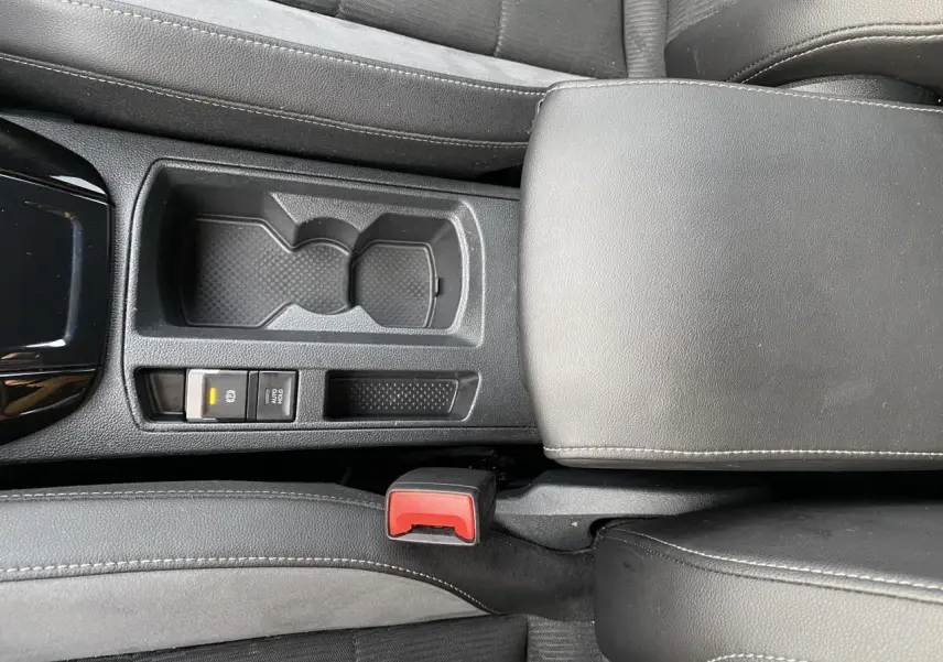 Vue rapprochée de la console centrale grise avec accoudoir en similicuir et bouton frein à main électrique du Volkswagen T-Roc 2024.