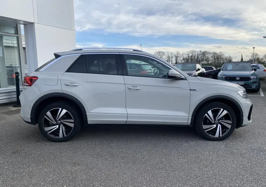Profil côté gauche d'un Volkswagen T-Roc gris clair 2024 avec jantes alliage bicolores et vitres surteintées.