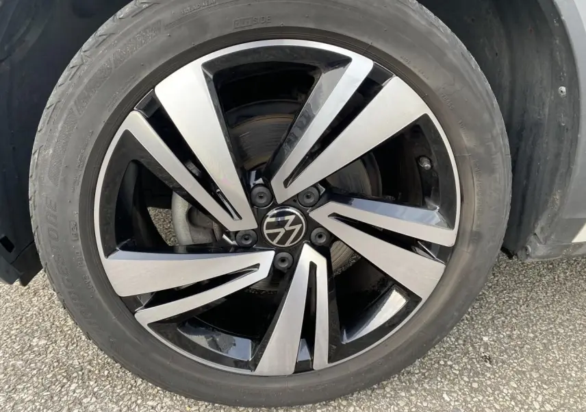 Gros plan sur la jante en alliage léger Nevada noire et brillante du côté avant droit d'un Volkswagen T-Roc gris.