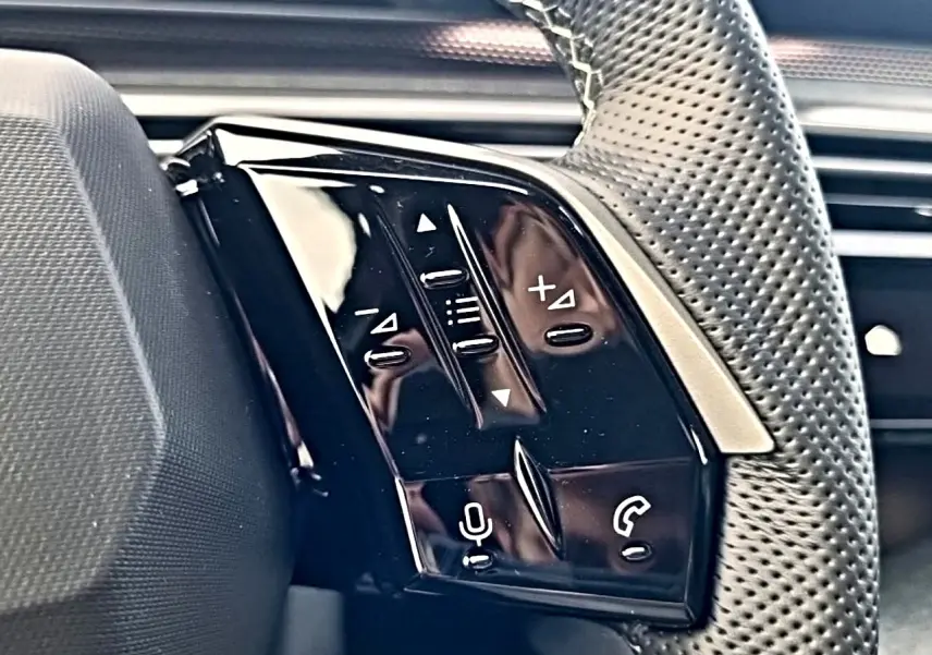 Gros plan sur les commandes noires du volant cuir perforé du Peugeot 5008 Hybrid 145 GT e-dcs6, côté gauche.