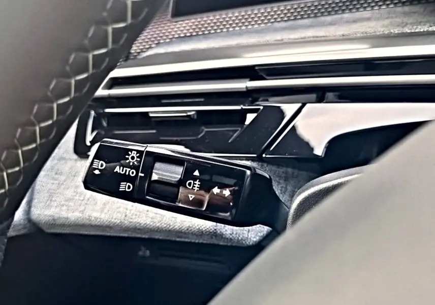 Gros plan sur la commande des phares et clignotants à gauche du volant du Peugeot 5008 Hybrid noir, intérieur moderne.