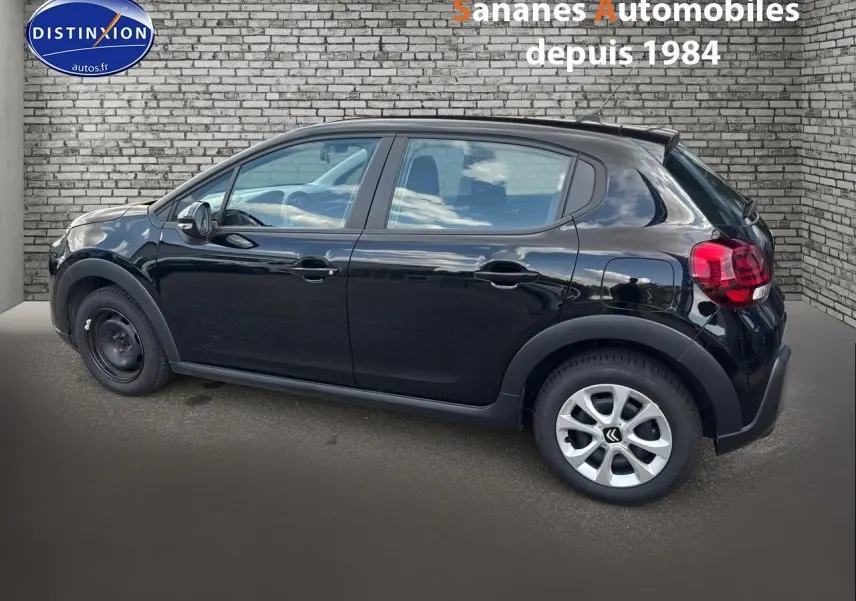 Profil côté gauche d'une Citroën C3 noire 2023 avec jantes alliage arrière et roue acier avant, devant un mur en briques.