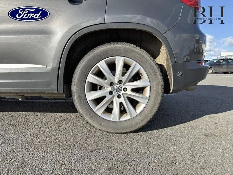 Gros plan sur la roue arrière droite d'un Volkswagen Tiguan gris Crypton, avec jante alu et logo VW visible.