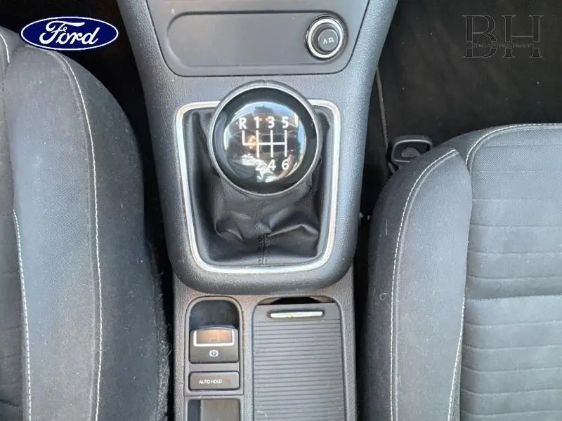 Vue plongeante sur le levier de vitesse manuel noir entouré de sièges tissu gris foncé, console centrale avec commandes.