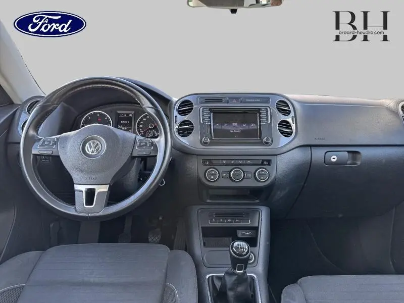 Vue intérieure avant du Volkswagen Tiguan 2016 avec tableau de bord noir, volant cuir multifonction et levier de vitesses manuel.
