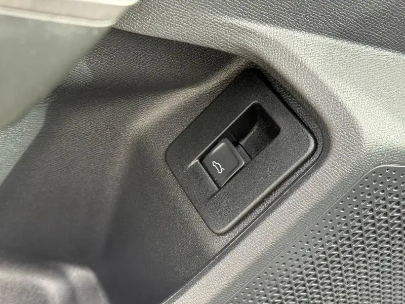 Gros plan sur le bouton d'ouverture du coffre côté conducteur dans l'habitacle du CUPRA Formentor blanc Nevada 2025.