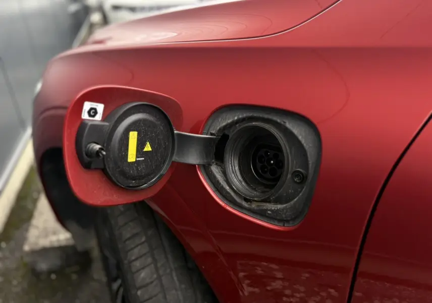 Prise de recharge ouverte côté gauche d’un Volvo XC60 T6 AWD PHEV 2024 rouge Fusion, détail du port de charge hybride.