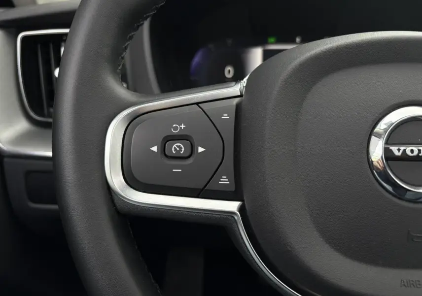 Gros plan sur la partie gauche du volant noir simili-cuir du Volvo XC60 2024 avec commandes de régulateur de vitesse.