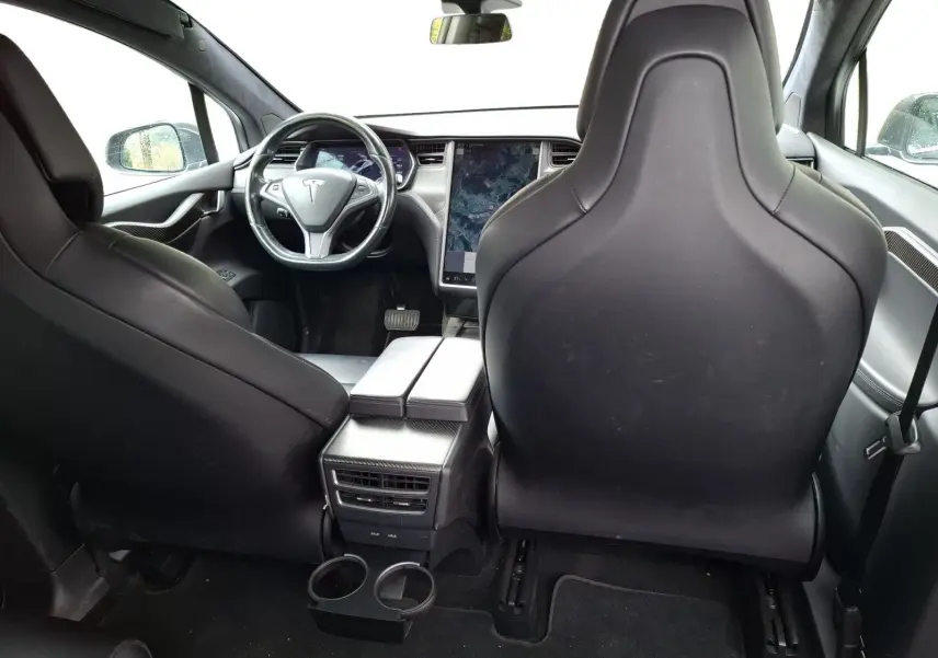 Vue intérieure arrière du Tesla Model X 100D gris foncé, montrant les sièges avant en cuir et l'écran tactile central vertical.