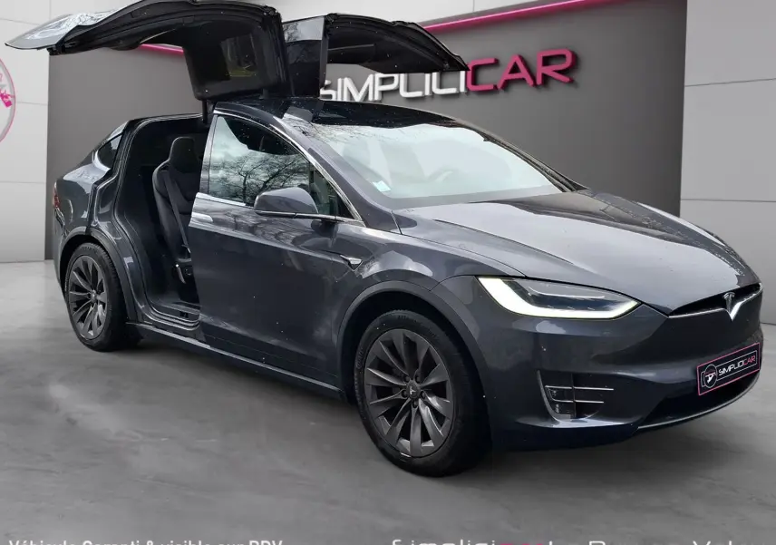 Tesla Model X 100D gris foncé en 3/4 avant droit avec portes papillon ouvertes, jantes alliage 20 pouces visibles.