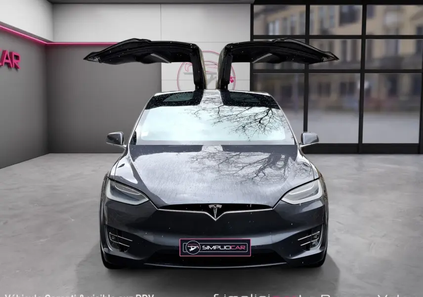 Vue frontale d’une Tesla Model X 100D gris foncé avec portes papillon ouvertes dans un showroom moderne.