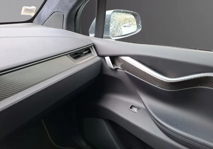Intérieur côté passager du Tesla Model X 100D 2018, montrant la porte avec insert carbone et tableau de bord gris foncé.