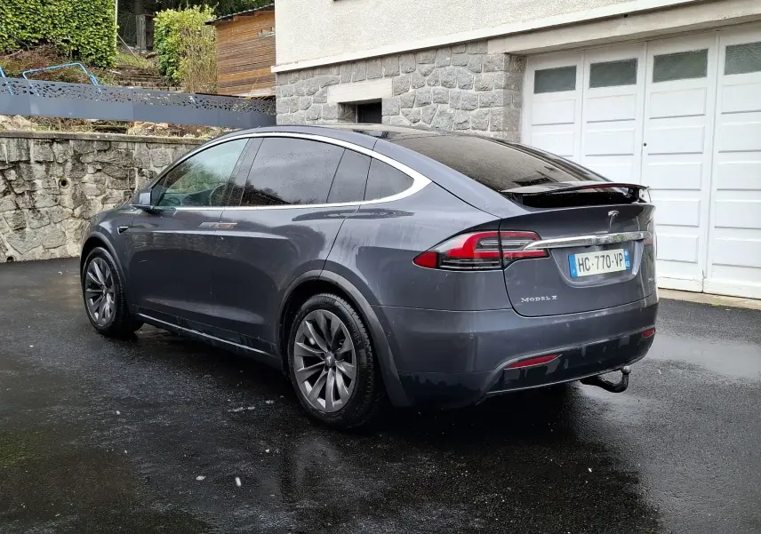 Tesla Model X 100D gris foncé vue 3/4 arrière droit, avec attelage et jantes alliage 20 pouces sous la pluie.