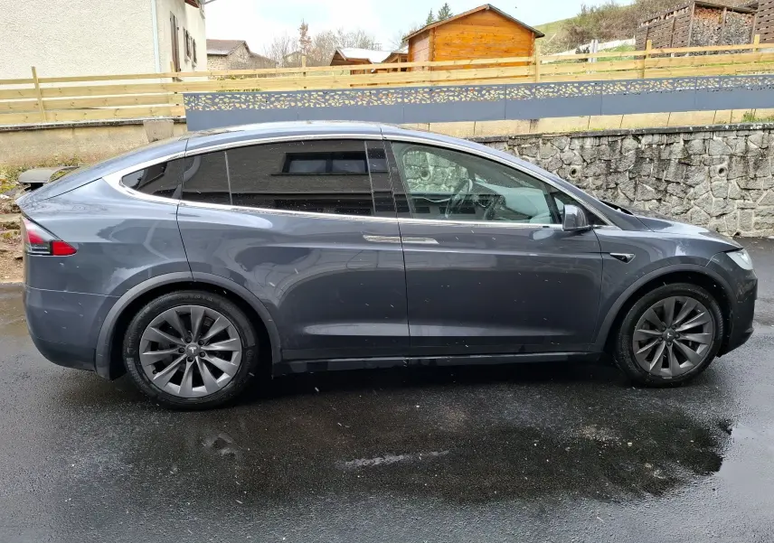 Tesla Model X 100D gris foncé vue de profil côté gauche sur sol mouillé avec jantes alliage 20 pouces et vitres teintées.