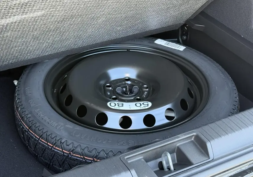 Roue de secours temporaire noire dans le coffre du Renault Captur gris Cassiopée, vue rapprochée du pneu sous plancher.