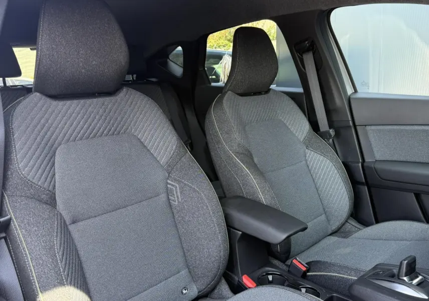 Vue intérieure sur les sièges avant gris texturés du Renault Captur 2026 avec accoudoir central et console de boîte auto.