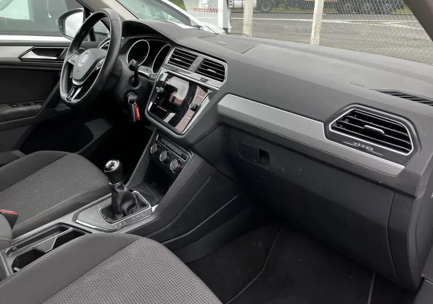 Intérieur côté conducteur du Volkswagen Tiguan blanc 2018, tableau de bord noir avec console centrale tactile et boîte manuelle.