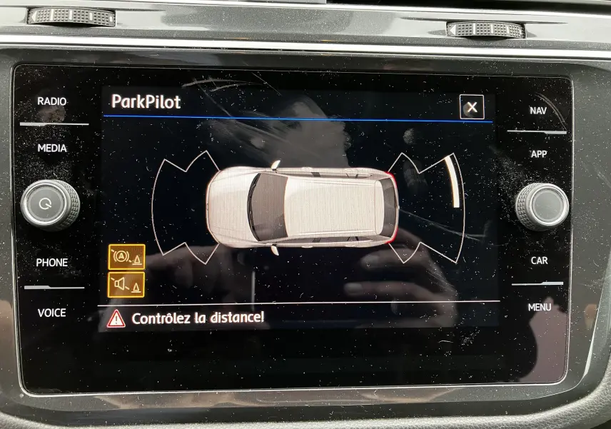 Affichage du système ParkPilot montrant un Volkswagen Tiguan blanc vu de dessus avec alertes de proximité sur l'écran central.