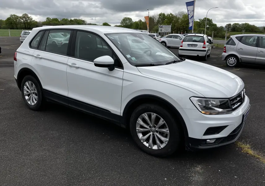 Volkswagen Tiguan blanc vu en 3/4 avant droit sur parking, avec jantes alliage et feux allumés.