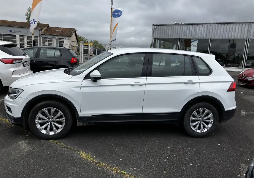 Profil côté gauche d'un Volkswagen Tiguan blanc 2018 stationné devant un bâtiment commercial sous ciel nuageux.