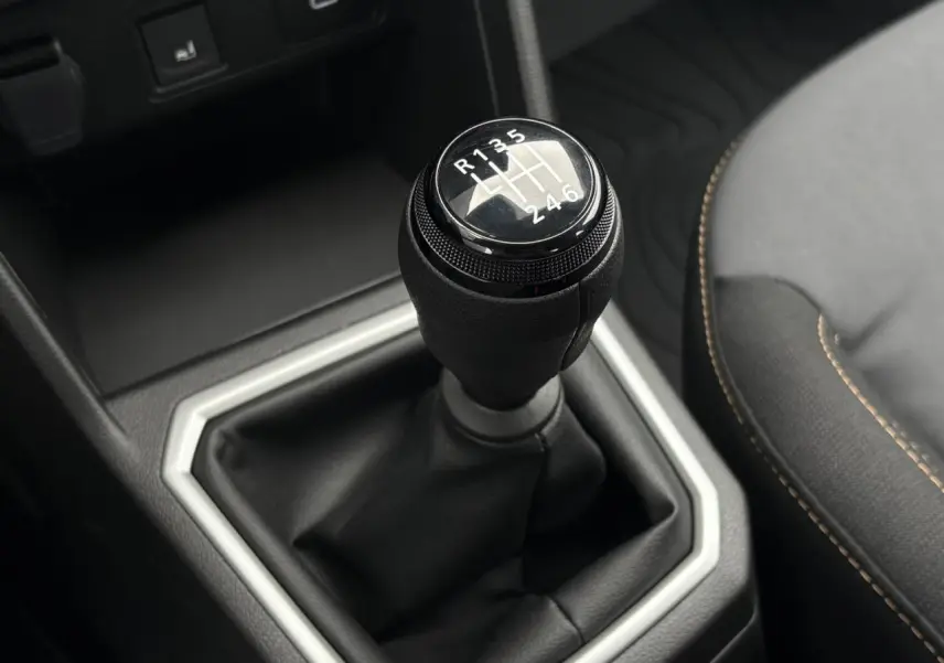Le levier de vitesses manuel noir de la Dacia Sandero Stepway 2025 vu en gros plan avec sellerie gris foncé et surpiqûres orange.