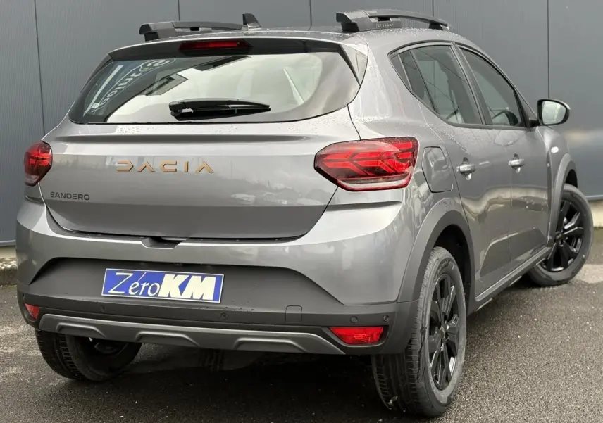 Vue 3/4 arrière droite d'une Dacia Sandero Stepway TCE 110 gris schiste avec barres de toit et jantes noires.