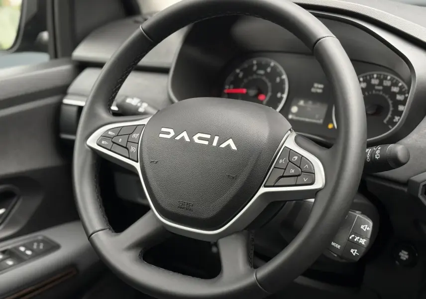 Gros plan sur le volant noir de la Dacia Sandero Stepway 2025, avec commandes intégrées et tableau de bord en arrière-plan.
