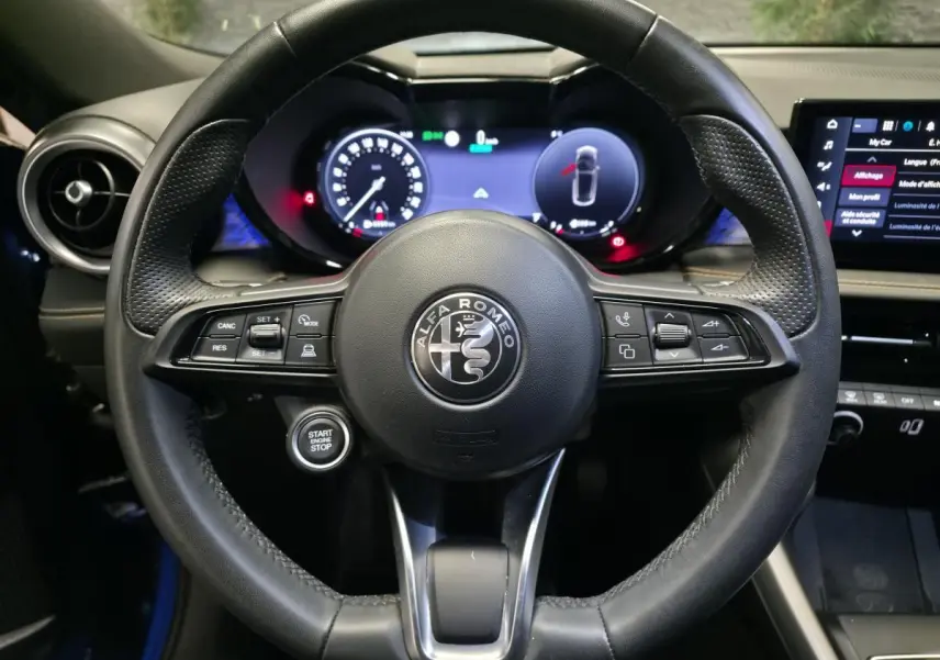 Vue centrée sur le volant sport en cuir noir de l'Alfa Romeo Tonale 2024, avec tableau de bord digital et bouton start/stop visible.