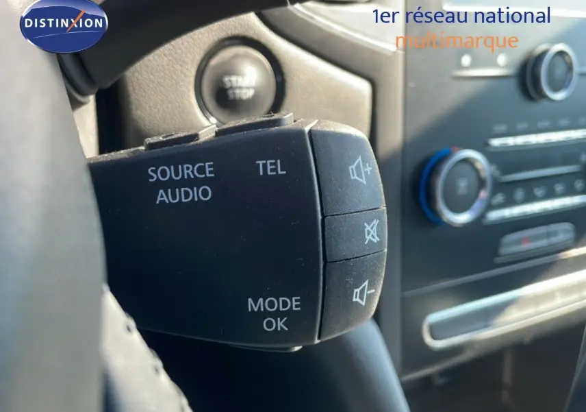 Gros plan sur la commande audio au volant d’une Renault Mégane bleu cosmos métal, intérieur noir visible en arrière-plan.