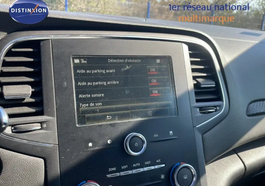 Vue rapprochée de la console centrale d’une Renault Mégane bleu cosmos métal, affichant les réglages d’aide au parking.