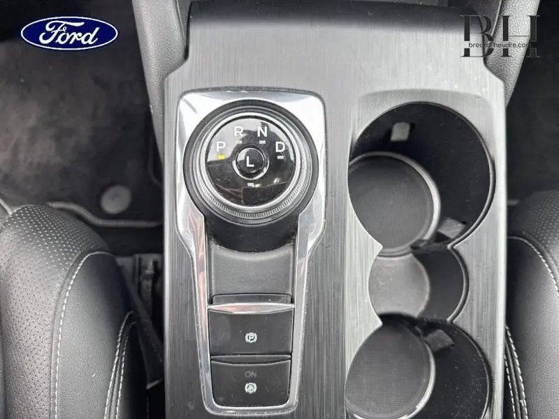 Vue plongeante sur la console centrale du Ford Kuga bleu azur, avec sélecteur rotatif de boîte auto et porte-gobelets.
