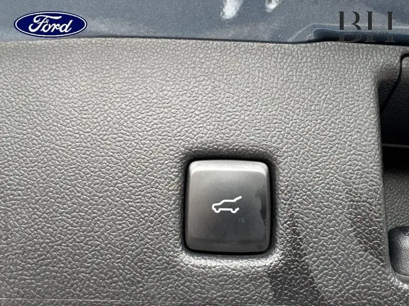 Bouton d'ouverture du coffre sur tableau de bord noir texturé du Ford Kuga bleu azur métallisé 2023.
