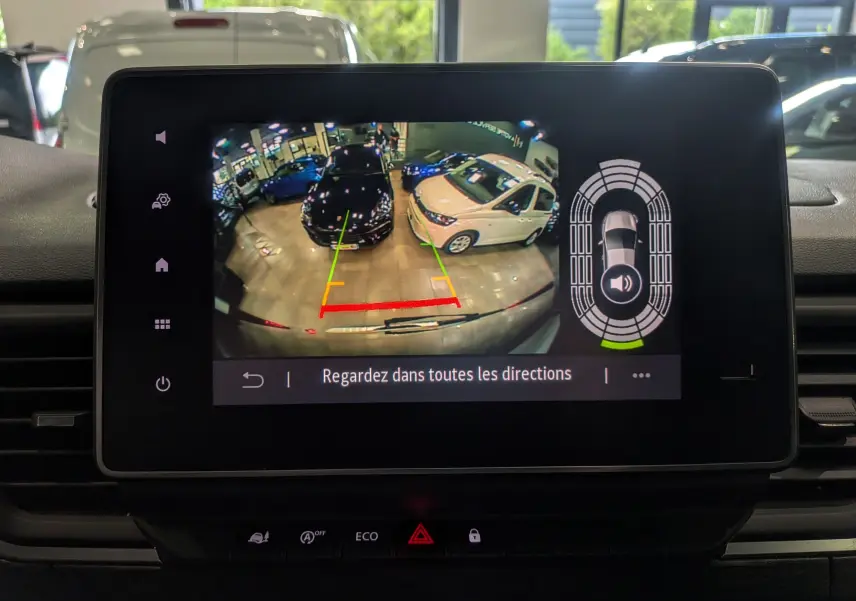 Écran de caméra de recul montrant le stationnement entre une voiture noire et une blanche dans un garage lumineux.