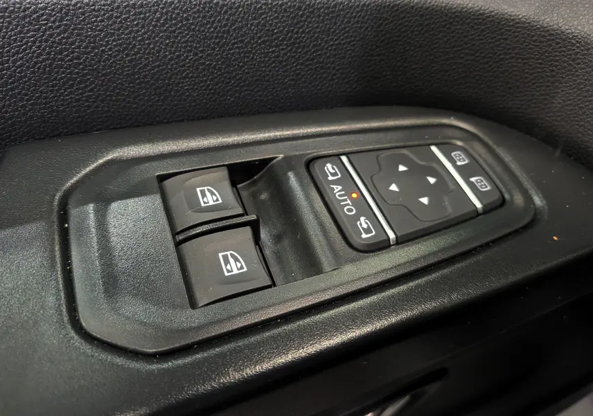 Gros plan sur les commandes électriques des vitres et des rétroviseurs du côté conducteur du Nissan Primastar Combi gris Highland.
