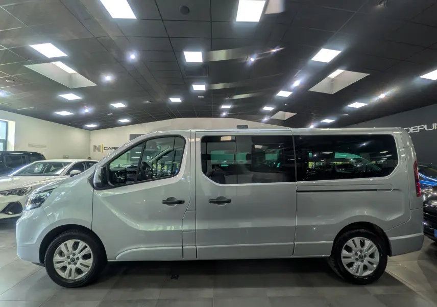 Vue de profil côté gauche du Nissan Primastar Combi gris Highland 2026 en showroom, avec vitres teintées et jantes alliage.