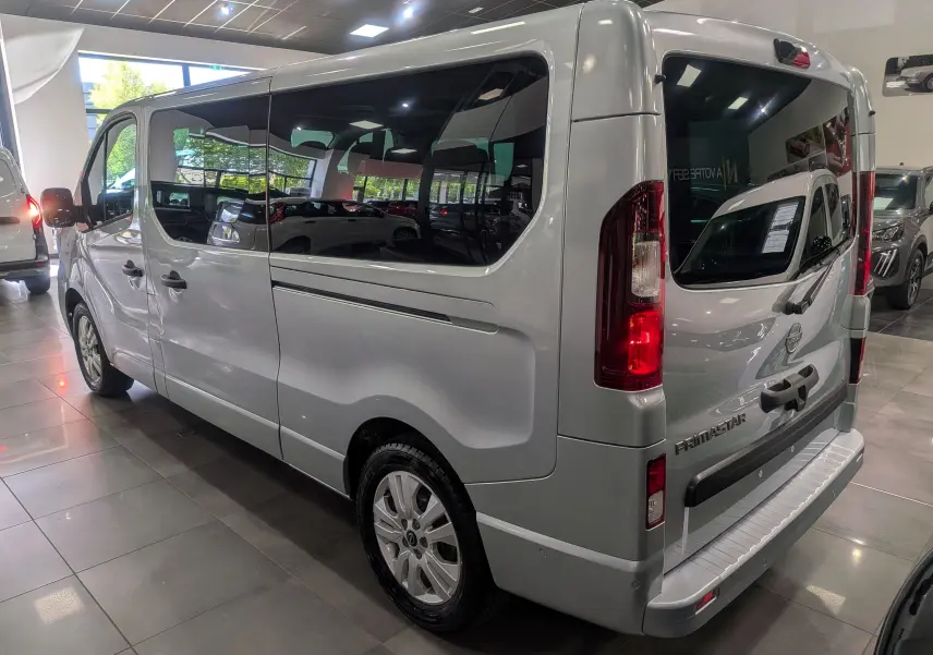 Vue 3/4 arrière droite du Nissan Primastar Combi gris Highland avec vitres teintées et feux arrière allumés en showroom.