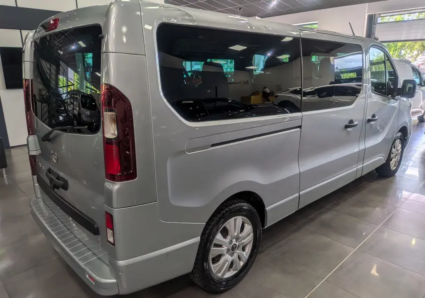 Vue 3/4 arrière droite du Nissan Primastar Combi gris Highland avec vitres teintées et jantes alliage en showroom.