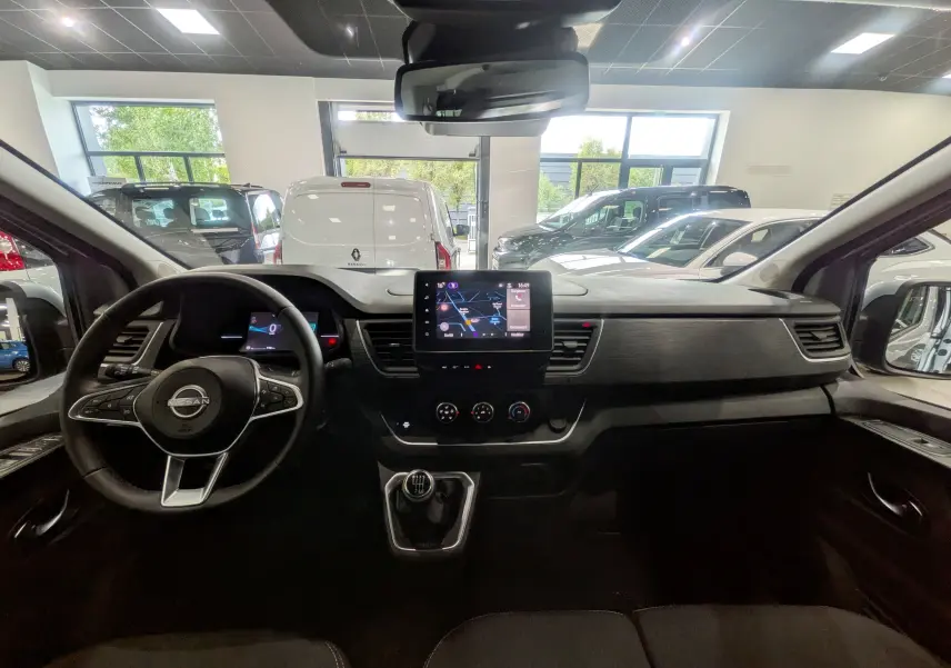 Vue intérieure avant du Nissan Primastar Combi 2026 gris Highland, avec tableau de bord moderne et écran tactile central.