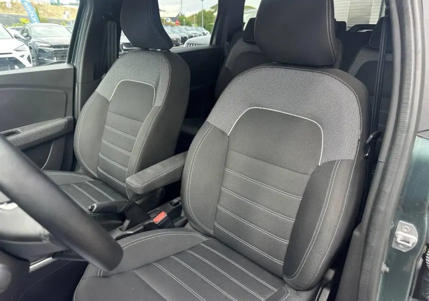 Vue rapprochée des sièges avant en tissu gris du Dacia Jogger vert cèdre, avec accoudoir central côté droit.