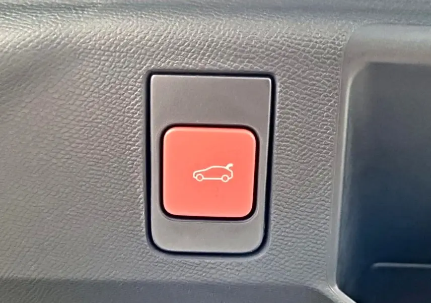 Gros plan sur le bouton rouge d'ouverture électrique du hayon dans l'habitacle d'un Peugeot 5008 noir.