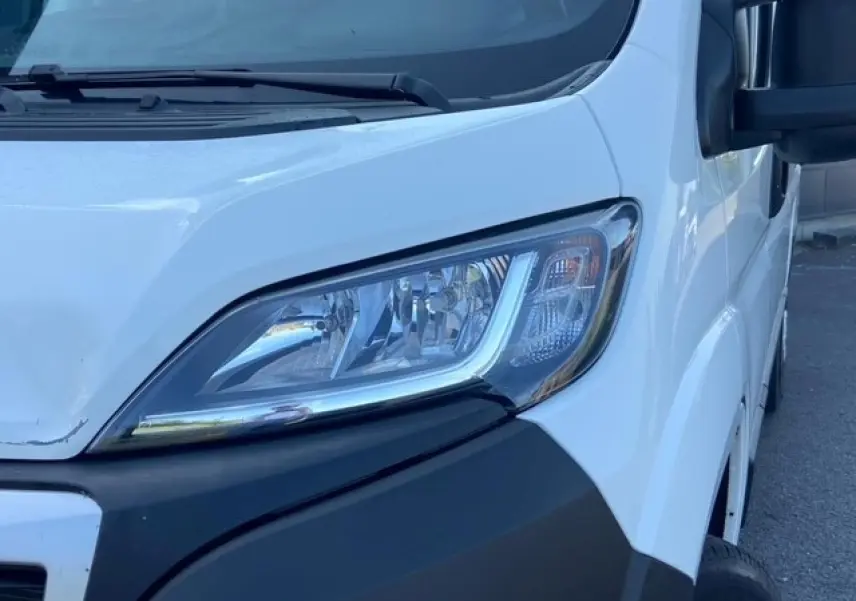 Gros plan sur le phare avant droit du Peugeot Boxer Fourgon blanc, soulignant la calandre et le rétroviseur noir.