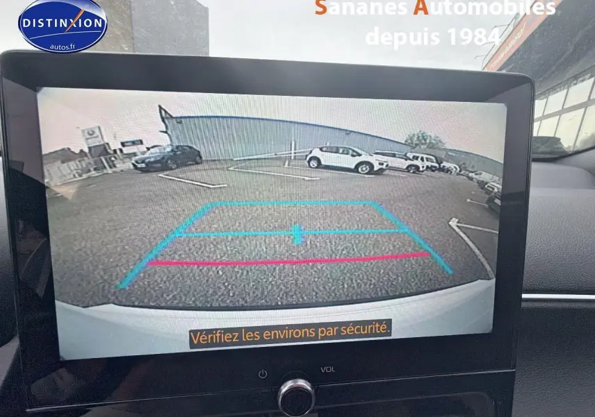 Écran tactile montrant la caméra de recul d'une Toyota Yaris Cross blanche, vue arrière avec lignes de guidage colorées.