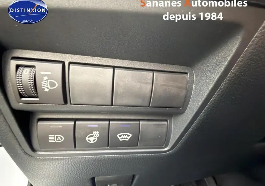 Gros plan sur les commandes de réglage d’éclairage et de chauffage du volant dans une Toyota Yaris Cross blanche, vue intérieure côté conducteur.