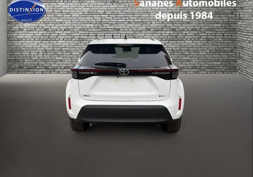Vue arrière d'une Toyota Yaris Cross Hybrid 130h blanche, avec feux arrière reliés par une bande noire et pare-chocs noir.