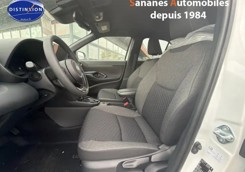 Vue intérieure côté conducteur de la Toyota Yaris Cross Hybrid blanche 2025, sièges tissu gris et volant multifonction.