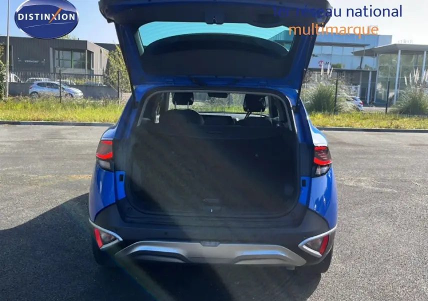 Vue arrière d'un KIA Sportage bleu fusion métal 2022 avec coffre ouvert, montrant l'espace de chargement et les feux arrière allumés.